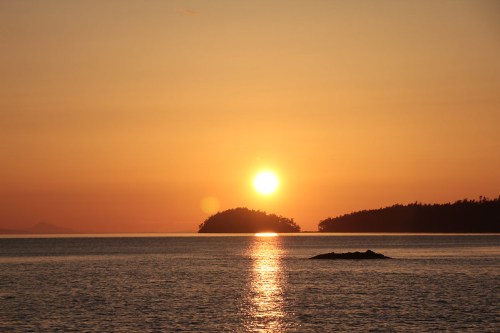 Sunset over calm waters, with a silhouette of an island and a warm orange sky reflecting on the surface.