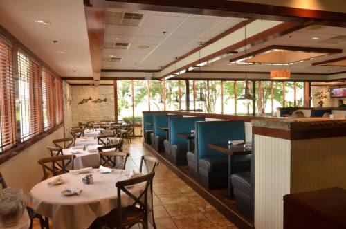 Interior of a restaurant featuring tables with white tablecloths and blue booths, surrounded by large windows.