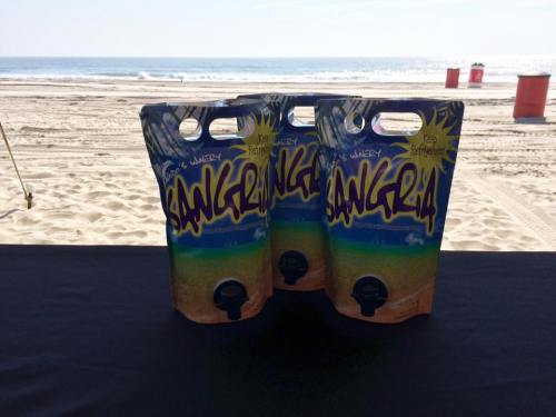 Three pouches of Sangria on a table with a beach and ocean in the background.