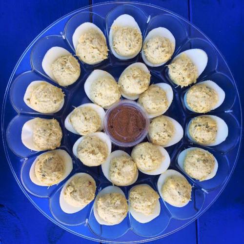 A circular platter of deviled eggs arranged neatly, with a small container of sauce in the center.