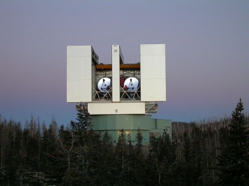 A large observatory structure with two domes, surrounded by trees and a twilight sky.