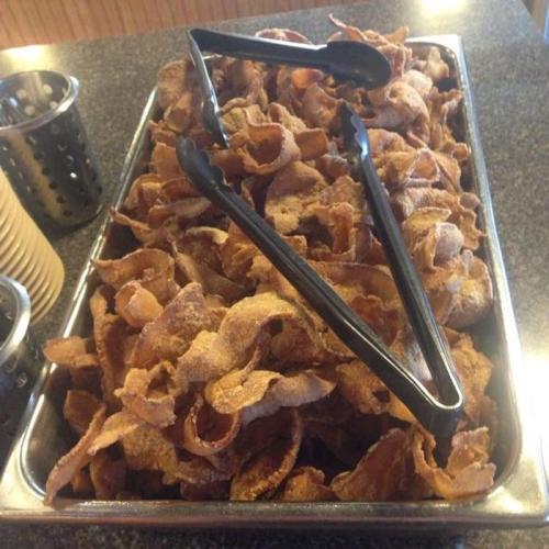 A metal tray filled with crispy, golden-brown pork rinds, with tongs resting on top.