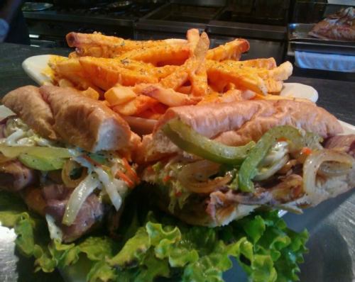 A plate with two sandwiches filled with meat and vegetables, served with a side of golden fries.