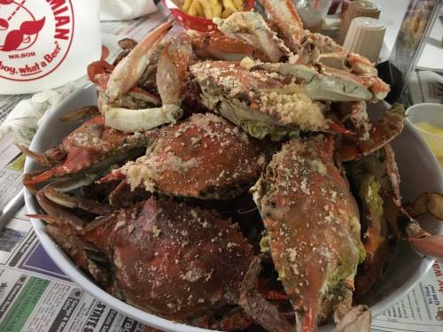 A large bowl filled with seasoned crabs, piled high, with fries and condiments in the background.