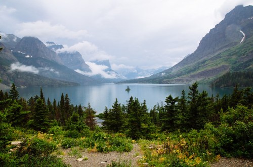 A serene lake surrounded by mountains and lush greenery under a cloudy sky.
