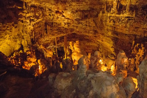 A dimly lit cave interior with illuminated rock formations and stalactites, creating a mystical atmosphere.