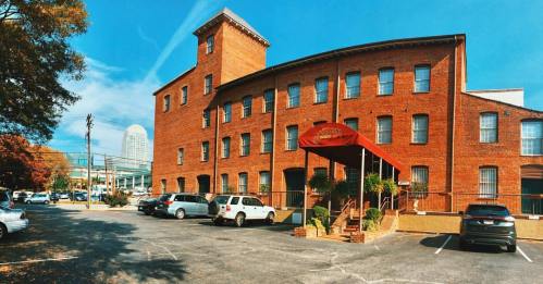 Historic red brick building with a canopy entrance, surrounded by parked cars and trees, under a clear blue sky.