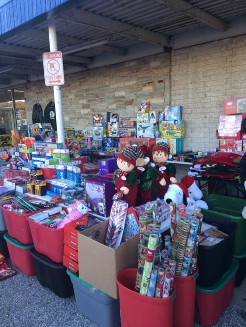 A festive display of holiday toys, decorations, and gift wrap outside a store, with two elf figures in the foreground.