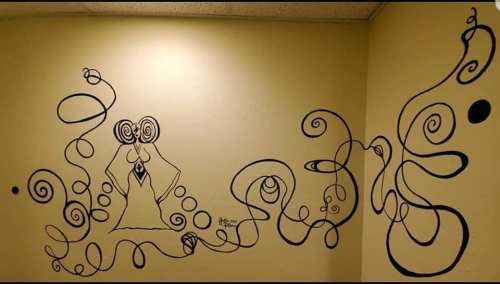 A whimsical black line mural on a yellow wall, featuring abstract swirls and a figure with spiral eyes.