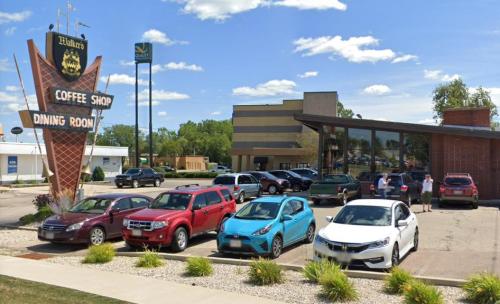 A coffee shop with a retro sign, surrounded by parked cars and people outside on a sunny day.