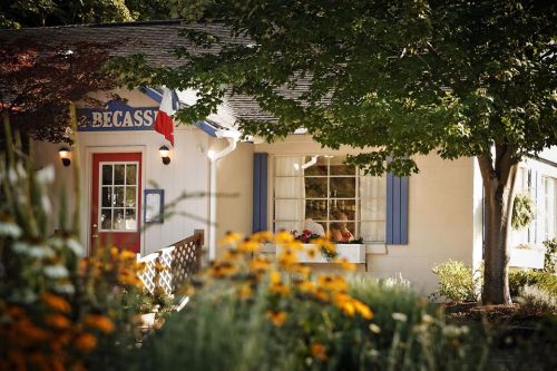 Charming restaurant exterior with blue shutters, a red door, and colorful flowers in the foreground.