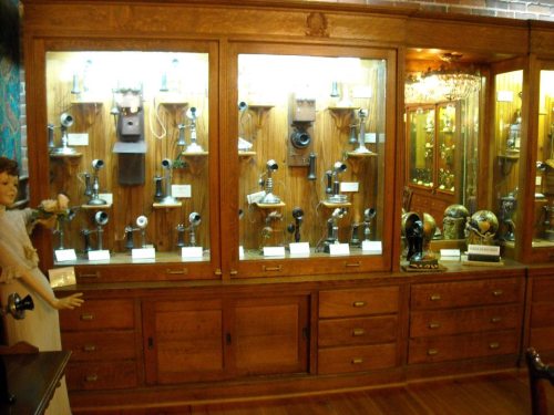 A display case filled with vintage telephones and antique items, showcasing various styles and designs.