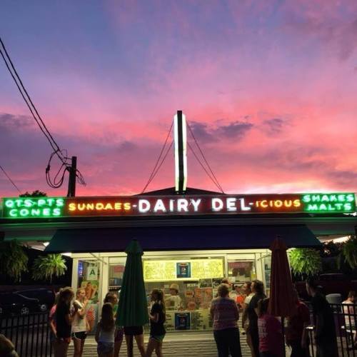A colorful ice cream shop at sunset, with a neon sign and a crowd of people enjoying the evening.