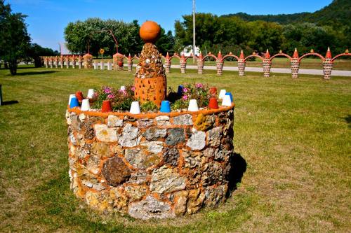 A decorative stone planter with colorful flower pots and a central sculpture, set in a grassy area with trees in the background.