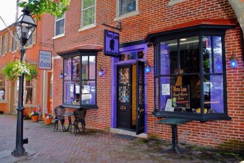 Charming brick storefront with purple accents, featuring outdoor seating and flower planters.