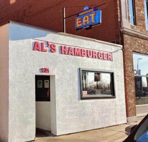 Exterior of Al's Hamburger restaurant, featuring a white wall, pink signage, and a blue "EAT" sign above.
