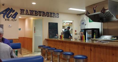 Interior of Al's Hamburgers, featuring a counter with stools, a menu board, and a cook in the kitchen area.