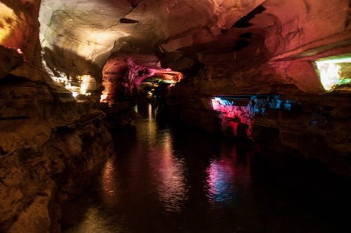 A dimly lit cave with colorful lights reflecting on the water, creating a mystical atmosphere.