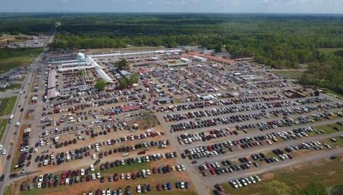 Aerial view of a large outdoor event with numerous cars parked and vendors set up in a sprawling area.