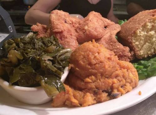 A plate of fried chicken, collard greens, sweet potato mash, and cornbread, served on a bed of lettuce.