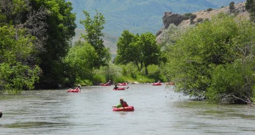 People floating on inflatable rafts down a calm river, surrounded by lush greenery and scenic hills.