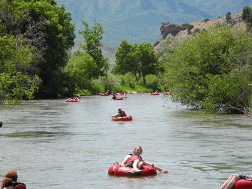 People floating on red inner tubes down a river, surrounded by lush greenery and mountains in the background.