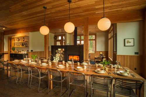 A spacious dining area with a long wooden table set for a meal, featuring a cozy fireplace and warm lighting.