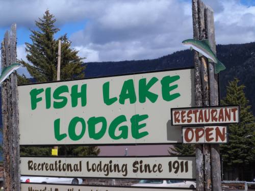 Sign for Fish Lake Lodge, featuring "Restaurant Open" and "Recreational Lodging Since 1911," surrounded by trees and mountains.