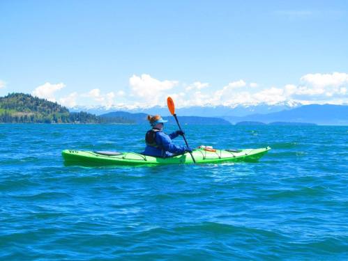 A person kayaking on a bright blue lake with mountains in the background and a clear sky.