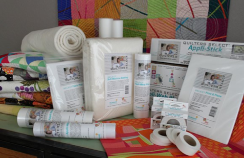 A variety of quilting supplies, including batting, fabric rolls, and appliqué products, arranged on a table.