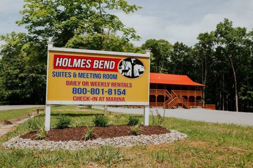 Sign for Holmes Bend Suites & Meeting Room, featuring contact info and rental details, set in a scenic outdoor area.