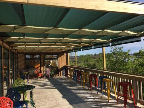 A spacious wooden deck with colorful chairs and tables, shaded by a green canopy, overlooking greenery and water.