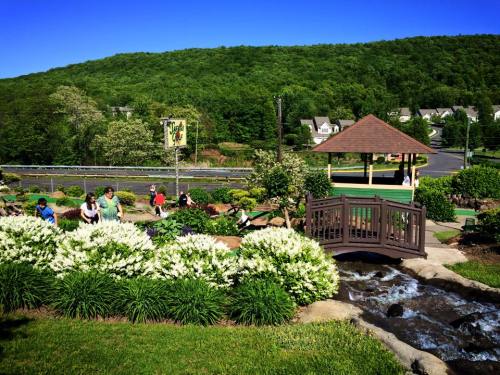 A scenic view of a park with a bridge, flowers, and people enjoying the outdoors on a sunny day.