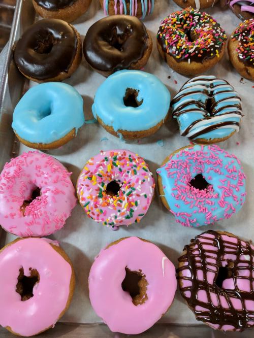 A variety of colorful donuts with chocolate, pink, and blue icing, topped with sprinkles and drizzles.