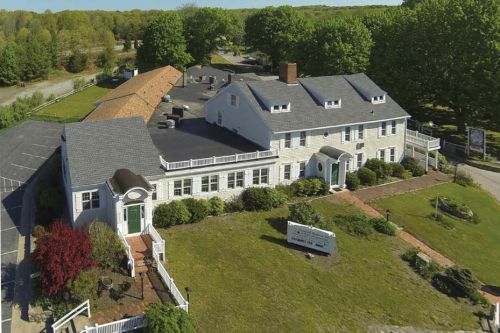 Aerial view of a large, white building with a green door, surrounded by trees and a parking area.