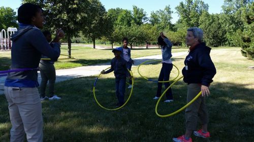 A group of people, including children and adults, are playing with hula hoops in a sunny park.