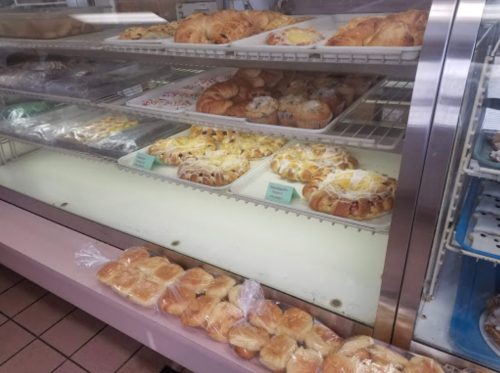 A display case filled with various baked goods, including croissants, muffins, and sweet rolls.