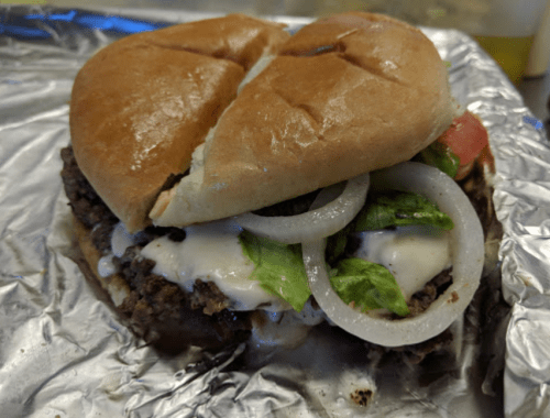 A close-up of a hamburger with lettuce, tomato, onions, and creamy sauce on a toasted bun, wrapped in foil.