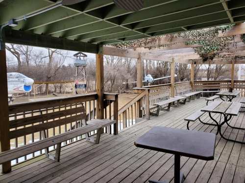 A wooden deck with benches and tables, overlooking a grassy area and a watchtower in the background.