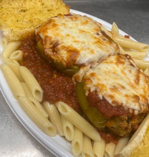 A plate of stuffed bell peppers topped with melted cheese, served with pasta, marinara sauce, and garlic bread.