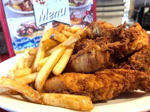 A plate of crispy fried chicken served with golden French fries, with a menu in the background.