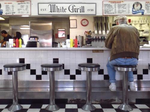 A diner scene featuring a man sitting at a counter with retro stools, surrounded by a menu and condiments.