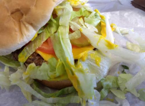 Close-up of a hamburger with lettuce, tomato, cheese, and mustard, nestled in a soft bun.