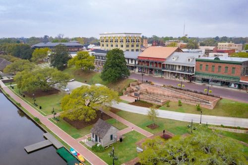 Aerial view of a riverside town featuring historic buildings, green spaces, and a calm waterway.