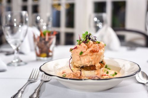 A gourmet dish featuring layered seafood atop a bed of vegetables, garnished with microgreens, on a white tablecloth.
