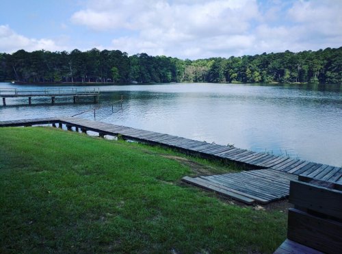 A serene lake surrounded by trees, with wooden docks extending into the water under a partly cloudy sky.
