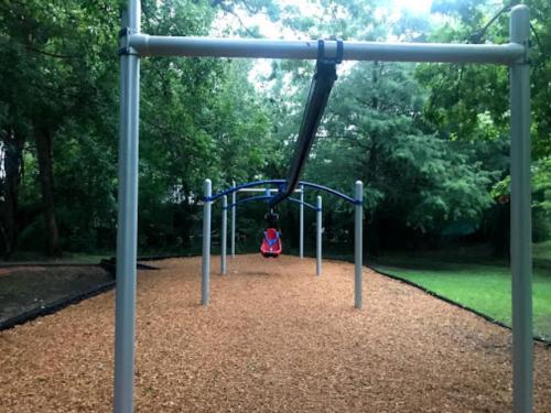 A playground with a swing set and a single swing, surrounded by trees and wood chip ground cover.