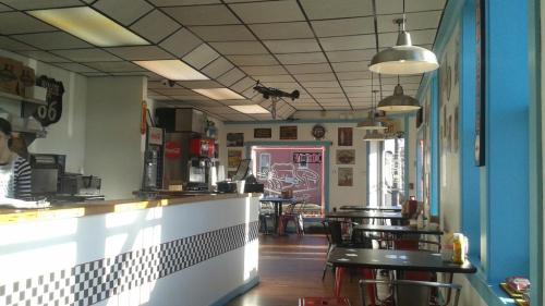 A retro diner interior with checkered decor, tables, and a counter, featuring vintage signs and a bright blue wall.