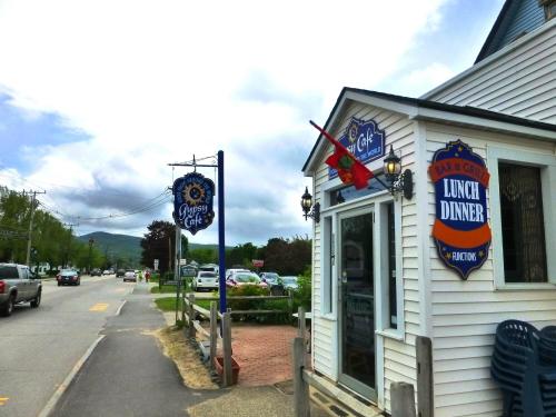A quaint café with signs for lunch and dinner, located on a street with cars and trees in the background.