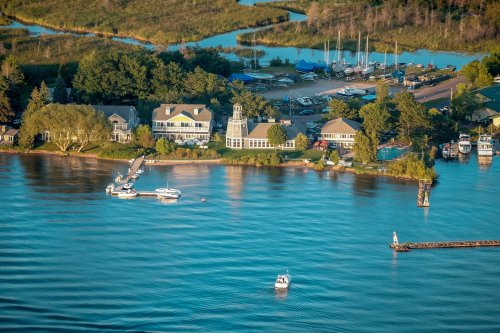Aerial view of a lakeside property with boats, lush greenery, and a calm water surface reflecting the surroundings.